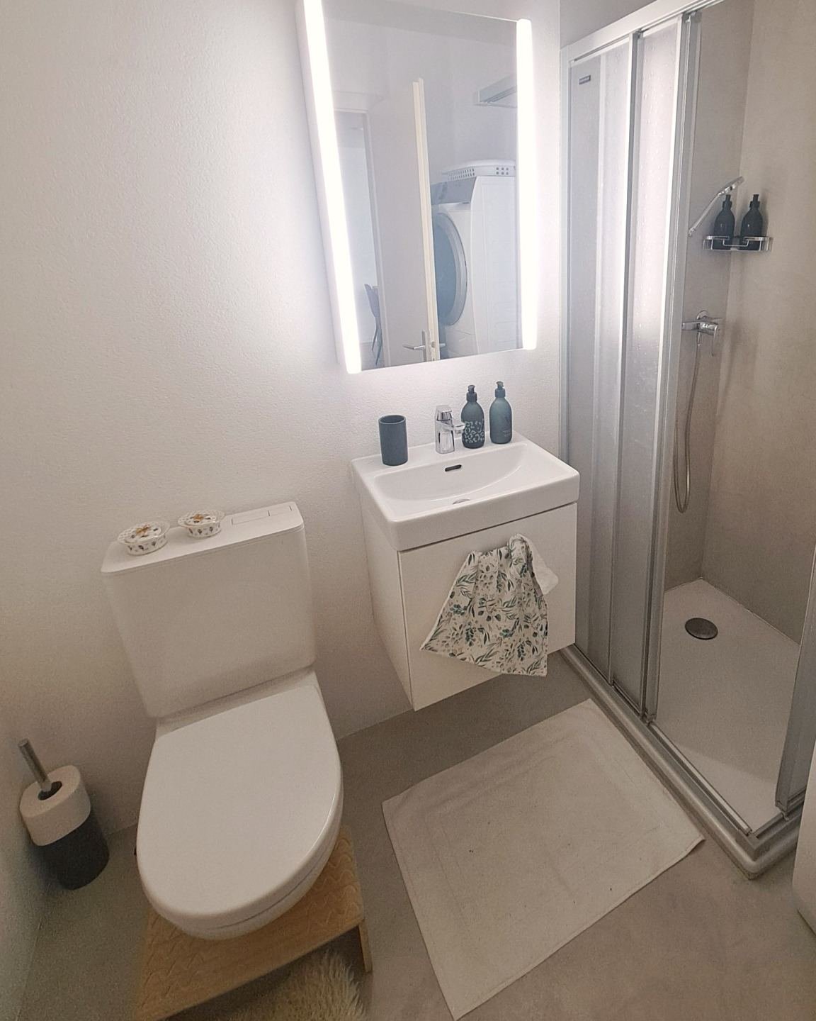 Salle de bain avec douche, lavabo et miroir éclairé